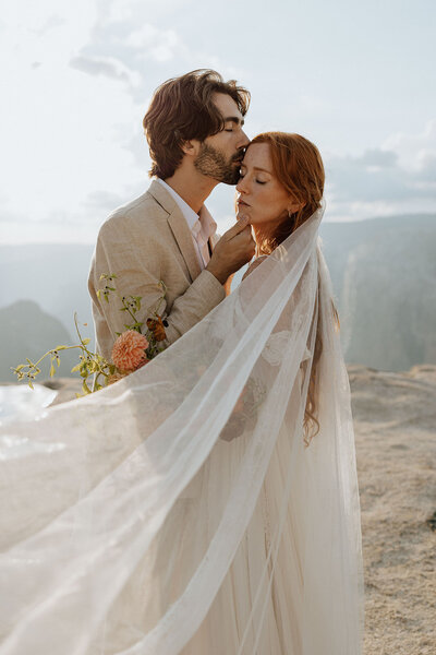 bride and groom embracing, groom kissing brides temple with veil flowing in front
