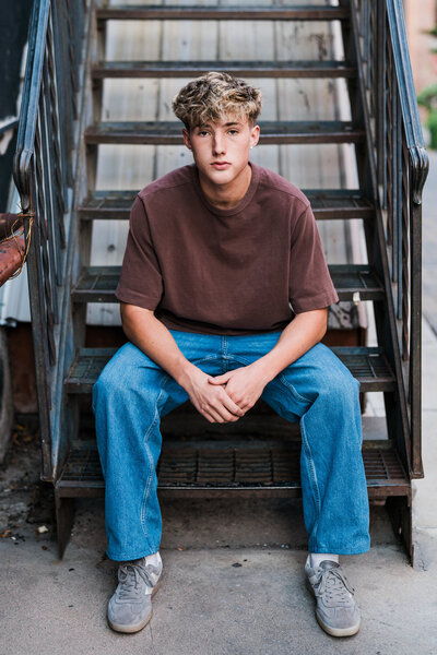 Colorado senior pictures of a boy sitting on outdoor stairs in casual clothes, captured by a Colorado Wedding and Portrait Photographer.