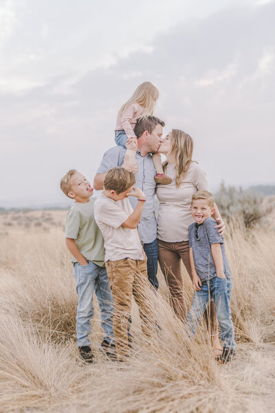 Joyful family of four laughing together in an open field, dressed in coordinating neutral tones for a warm and timeless look.