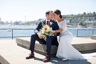 Bride and groom embrace on balcony in front of water