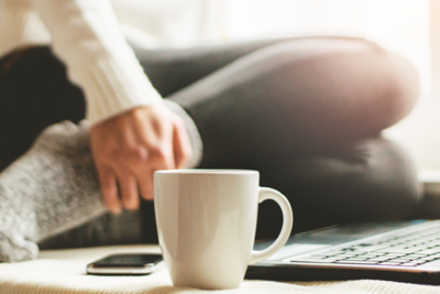 Coffee mug beside a laptop in a relaxed home setting, representing reflective space and intentional living.