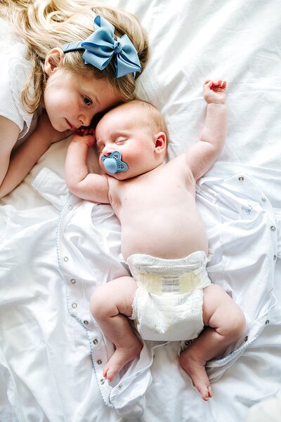 big sister and newborn baby laying on a bed