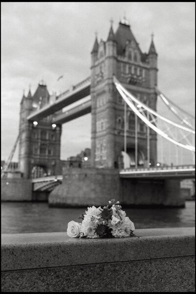 A filmy black and white photo of a wedding bouquet with the Tower Bridge in London in the background.