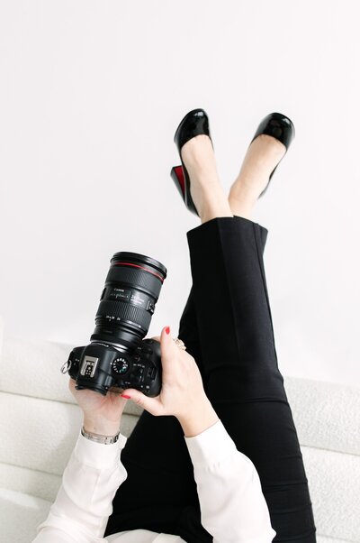 Creative brand portrait of Colorado wedding photographer Logan Ferree lying on a white couch with louboutins kicked in the air, holding a camera — Mrs. Ferree Photography.