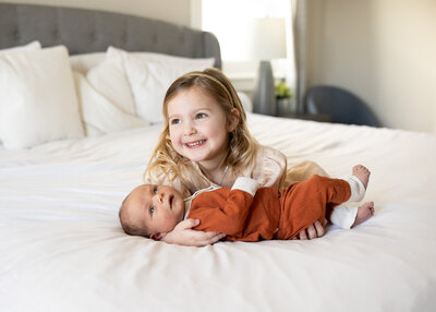 Sibling holding baby brother on bed smiling at parents.