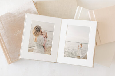 Flat lay of a handcrafted matted photo album featuring a serene portrait of a mother holding her baby by a calm lake. This heirloom-quality album is offered to Kansas City clients of Meredith Maag Photography, showcasing timeless and meaningful family moments.