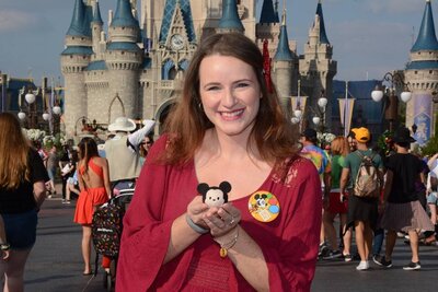 Amy Hord smiling and holding a Mickey Mouse tsum tsum in front of Cinderella's castle at Walt Disney World.