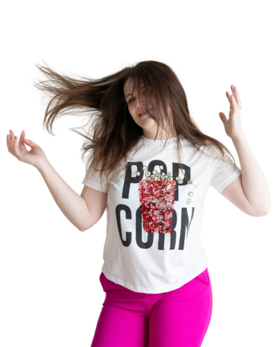 Emily wearing hot pink pants and a shirt that says pop corn with an image of glittery popcorn on it. She is flipping her hair in the air with her eyes closed and arms up in the air