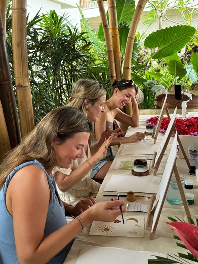 A group of women smiling and painting during an art therapy session in Bali. 