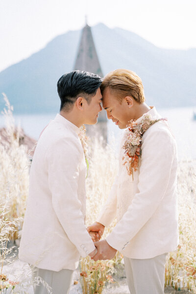 Emotional moment between two grooms holding hands during their wedding ceremony, surrounded by mountain views and soft natural light