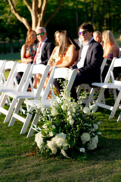 white chairs in rows with floral arrangement sitting in grass