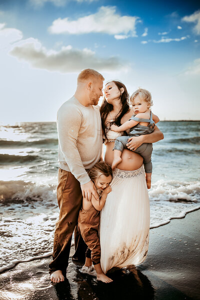 Family Photographer, a young family of four huddles together on the beach