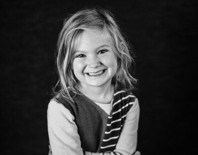 A school aged girl crosses her arms low on her chest and smiles naturally at the camera in Minneapolis on her school's portrait day.