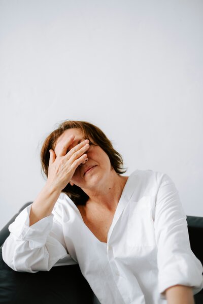 Frustrated woman in white shirt holding head in hand on couch