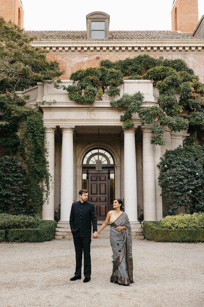 couple at filoli estate holding hands in front of large estate home, woman wearing indian sari