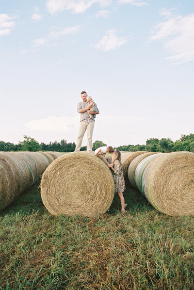 Family of four playing on hay bales in a grassy field