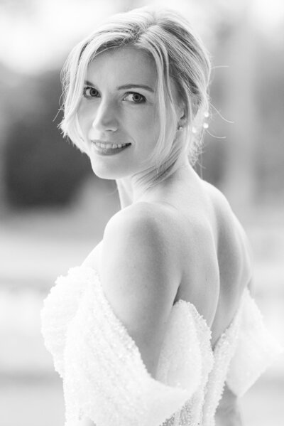 Black and white image of a bride in a white sparkly gown, the bride is looking back over her shoulder and the image is of the waist up