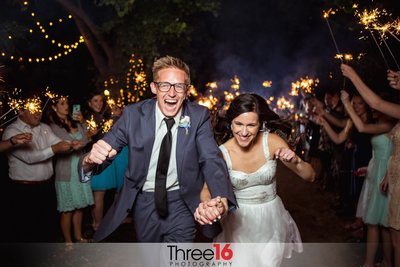 Bride and Groom exit the reception with big smiles on their faces as they go under a tunnel of lit sparklers held by wedding guests