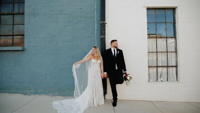 A Texas bride and groom pose in front of a blue building captured by a wedding videographer.