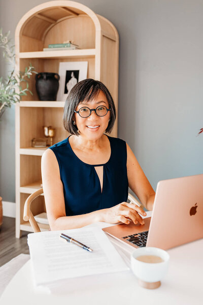 Woman working on a laptop at a desk, with a notepad and coffee mug nearby