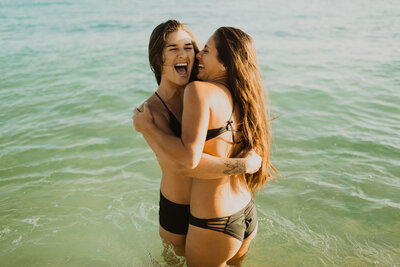 Couple hugging and laughing standing in the ocean in their swimsuits