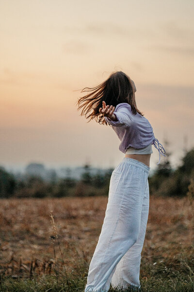 Tessa Adrian in einer Yoga-Pose auf einem Feld, Natur im Hintergrund.