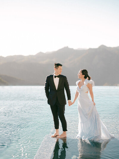 Man in Tux and Woman in beautiful long dress standing in lake with mountains in the background
