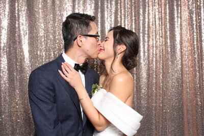 Couple kissing in front of champagne pink photo booth backdrop