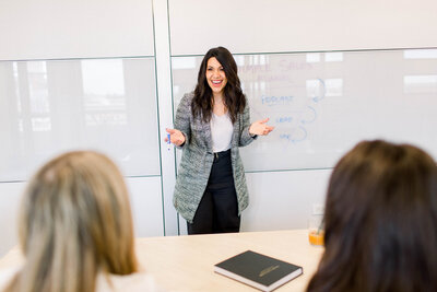 dark haired woman teaching a live workshop with grey blazer on