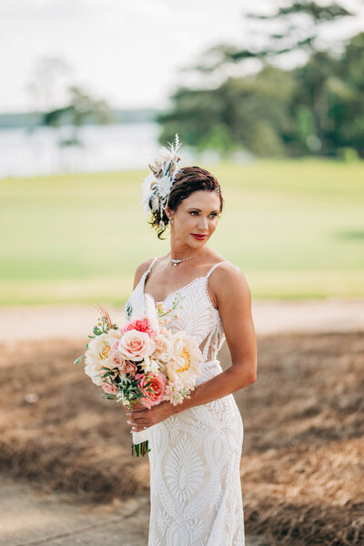 woman in white dress with flower in her hair holding a bouquet smiling