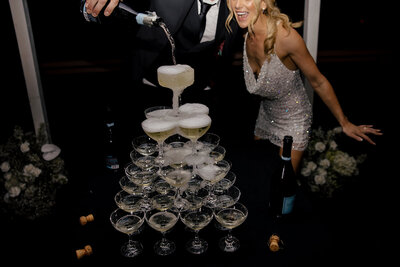 couple in suit and sparkly dress pour champagne over their champagne tower