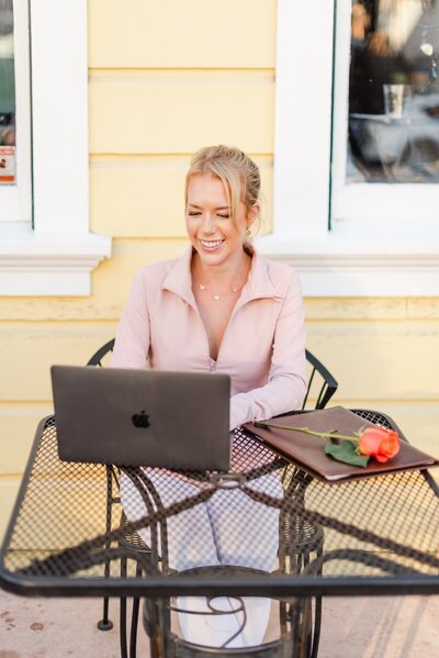 Woman sitting at outside cafe typing on laptop