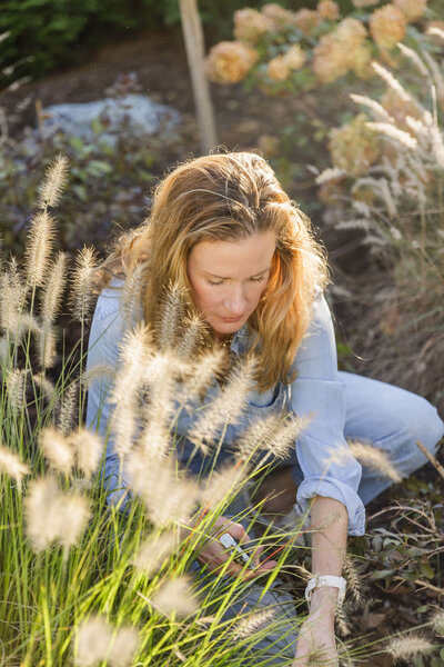 Woman kneeling in dirt among ornamental grass as she fixes up landscaping