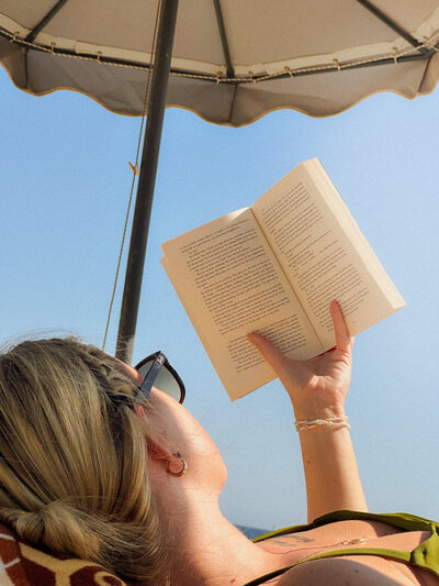 A woman holding a drink while reading a book. Showing that with anxiety therapy in Manhattan you can calm the inner chaos. An anxiety therapist can help you learn to relax and enjoy every day.