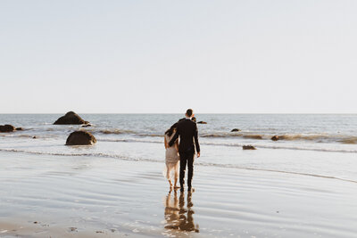Wedding couple walk barefoot into the water at beach