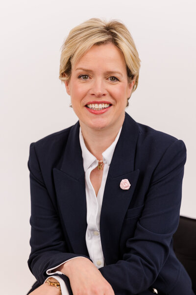 woman with short blonde hair sitting in front of white background wearing corporate outfit white shirt and dark blue jacket during headshot photoshoot with Laure Photography