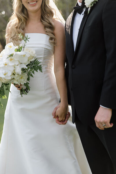 Bride and groom hold hands with the bride's bouquet