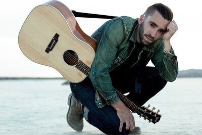 Musician photo Michael Bernard Fitzgerald on one knee in desert resting on one hand other hand resting on knee with guitar