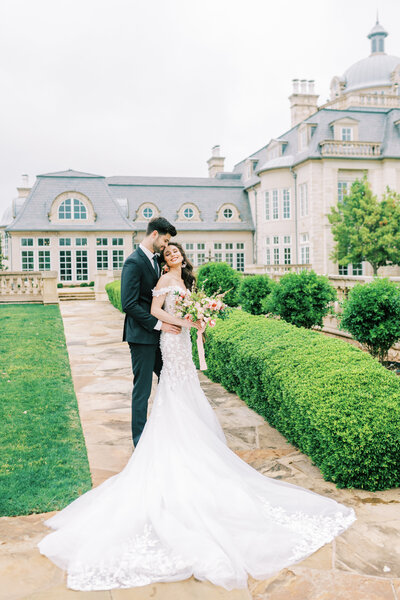 Bride and groom posing together and smiling in front of a large wedding venue