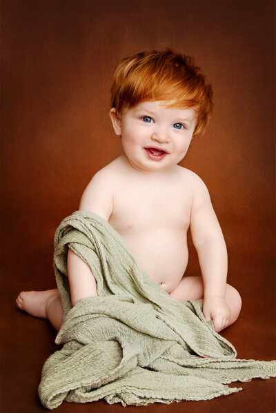 Red head boy posing with a light green blanket smillng at the camera