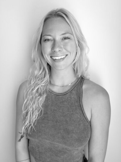 Black and white photo of blonde, female yoga instructor smiling at the camera.