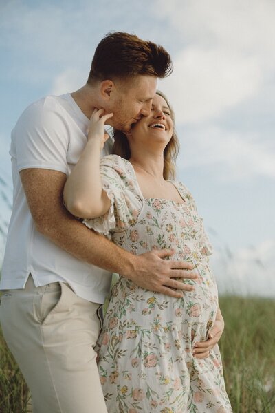 couple poses on the beach for maternity photos