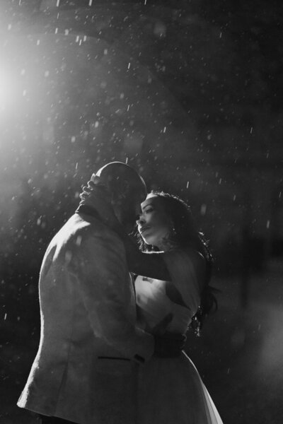 Bride and groom embrace in the rain at night under dramatic lighting at a luxury Isle of Wight wedding venue, capturing an intimate and elegant moment.