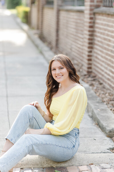 girl sitting on the sidewalk in a yellow blouse and jeans