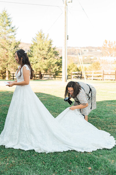 A photographer helping a bride fan out her dress