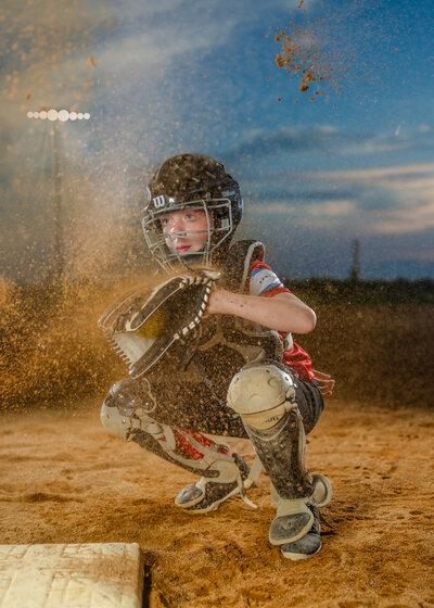 A young catcher catches the ball as dust flies through the air. 