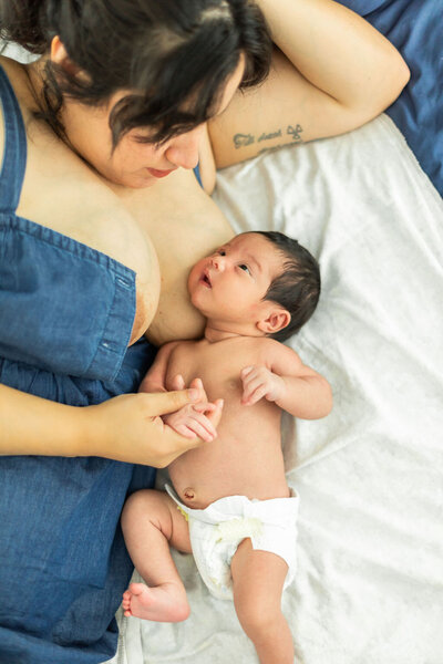 Newborn at home session taken in a neutral home in Kingwood, Texas with the mother in a blue jean dress while baby rest on her mother's chest ready to nurse