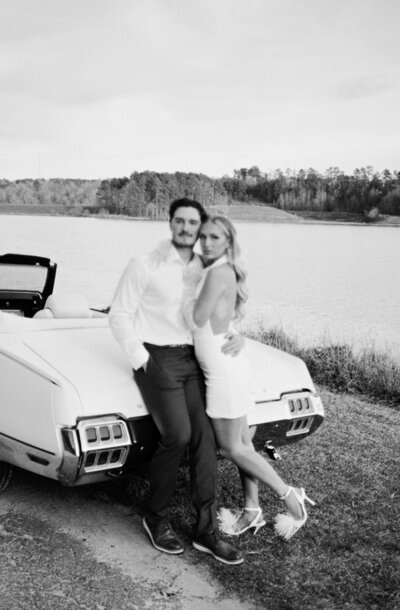 Newlyweds snuggle while leaning on the back of a vintage muscle car convertible 