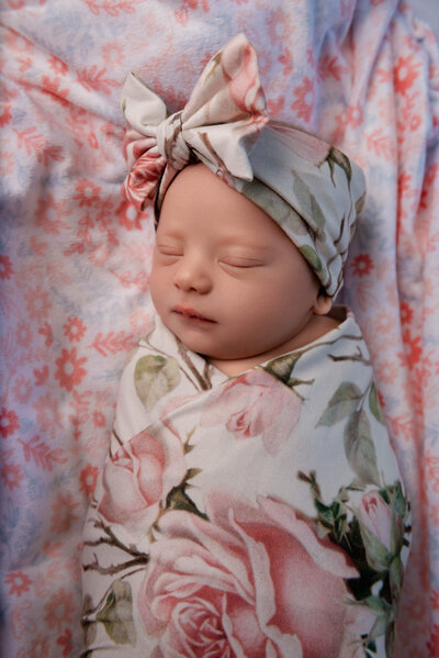 Newborn baby girl in pink rose swaddle with matching head bow