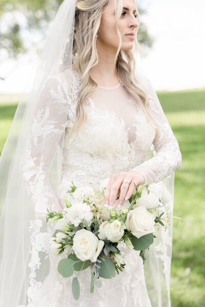 Bride looking off while gracefully touching her bridal bouquet.